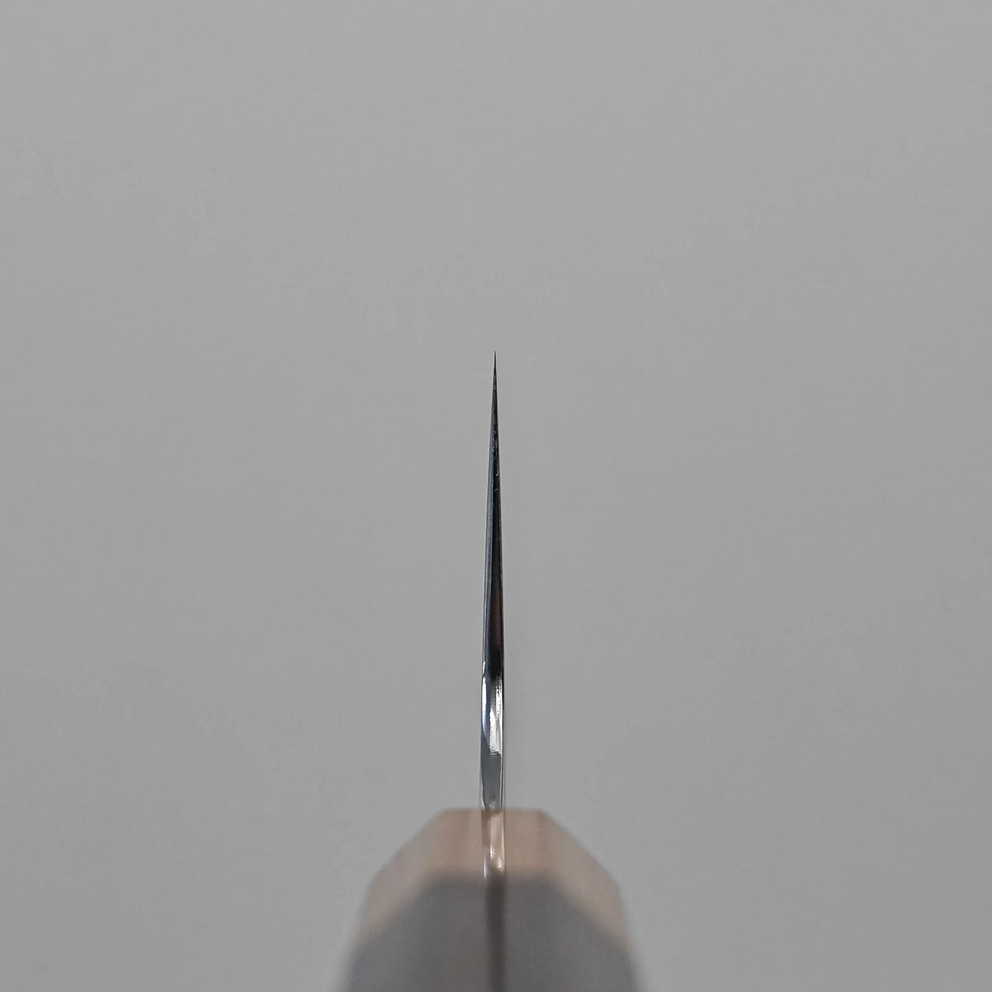 Close-up of the sharp edge on a Kei Kobayashi SG2 damascus gyuto 240mm chef knife blade, photographed from the tip against a neutral gray background. The blade is straight and features a polished, damascus surface.