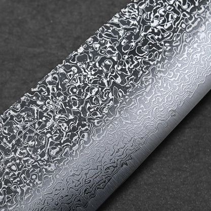 Close-up of the Kei Kobayashi SG2 damascus gyuto 240mm blade, highlighting intricate wavy and mottled patterns on the metal surface, set against a dark, textured background.