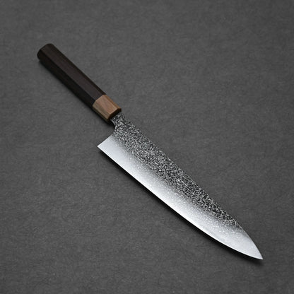 The Kei Kobayashi SG2 damascus gyuto 240mm, featuring a textured, speckled blade and dark wooden handle, rests on a dark gray surface to showcase the elegance of traditional Japanese craftsmanship.