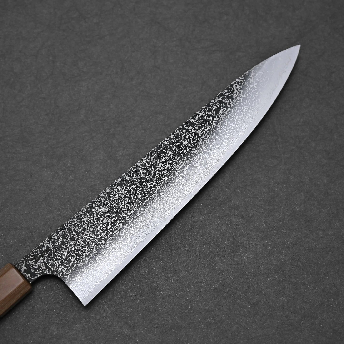 A close-up of the Kei Kobayashi SG2 damascus gyuto 240mm showcases its patterned Damascus steel blade and wooden handle on a dark textured surface, reflecting exceptional kitchen precision and craftsmanship.