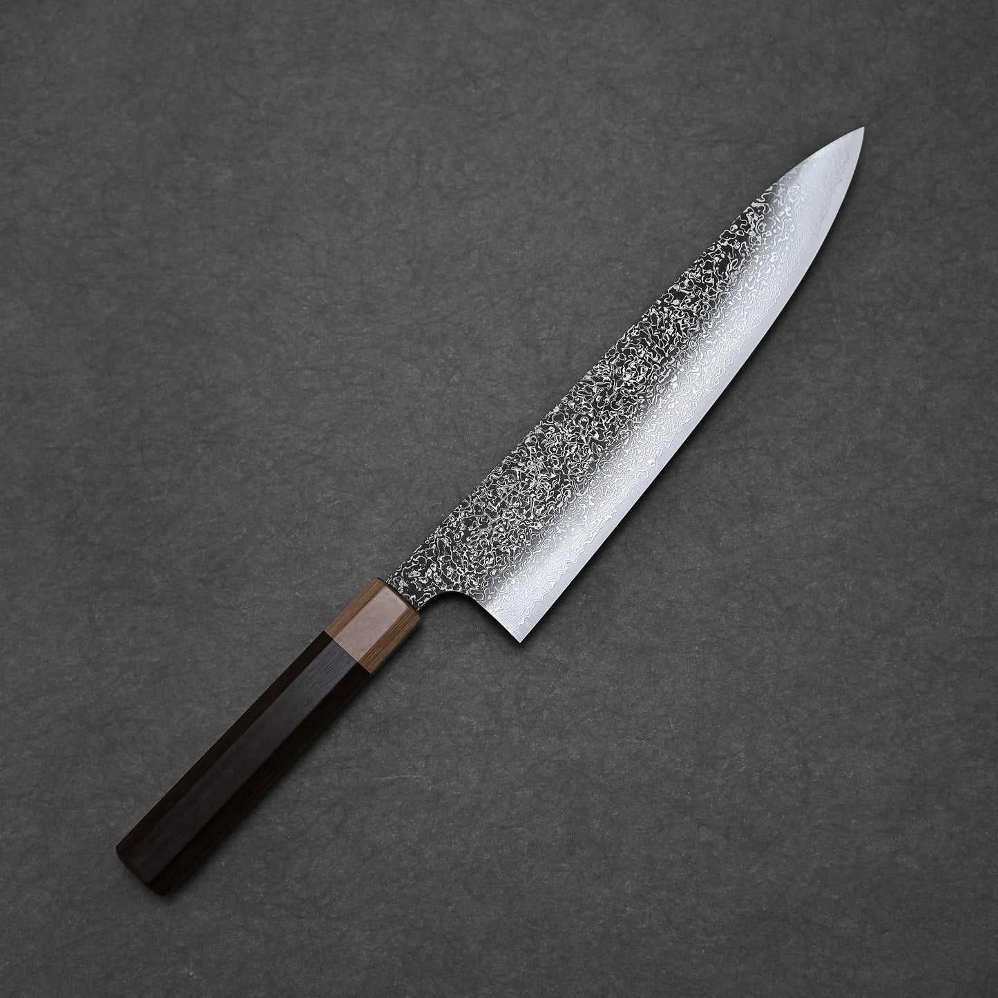 The Kei Kobayashi SG2 damascus gyuto 240mm features a speckled, textured blade and a dual dark wood handle, shown diagonally on a dark gray textured background.