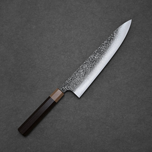 The Kei Kobayashi SG2 damascus gyuto 240mm features a speckled, textured blade and a dual dark wood handle, shown diagonally on a dark gray textured background.