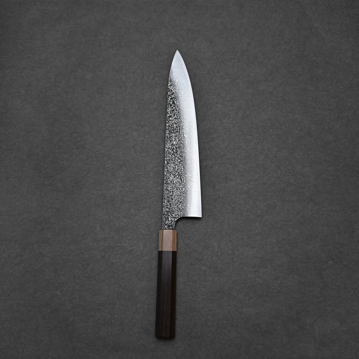 A Kei Kobayashi SG2 damascus gyuto 240mm chef knife with a textured blade and dark wooden handle is displayed on a plain dark gray surface.