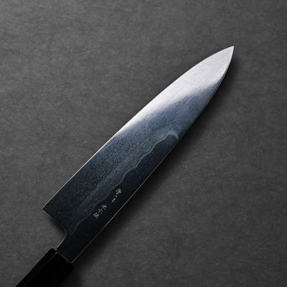 A gyuto Japanese knife with a long, gently curved blade and a dark handle is shown, blade finish not clearly visible.
