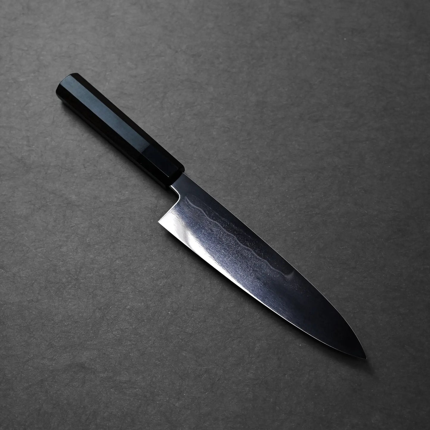 A dark-handled Japanese knife with a broad, curved blade and polished finish typical of a chef’s knife.