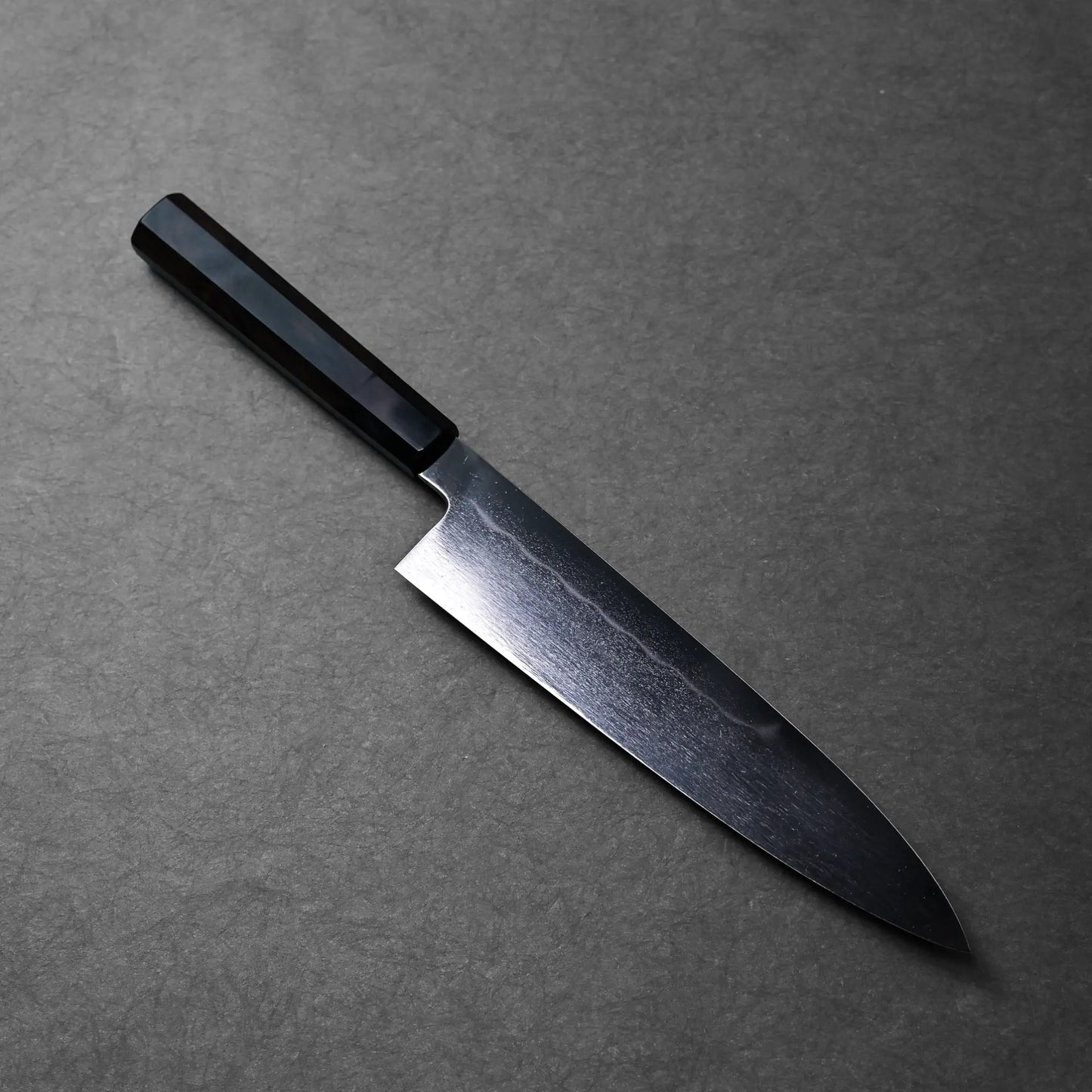 A gyuto Japanese knife with a black handle, visible curved edge and polished blade finish.