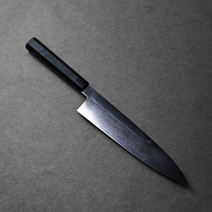 A gyuto Japanese knife with a black handle, visible curved edge and polished blade finish.