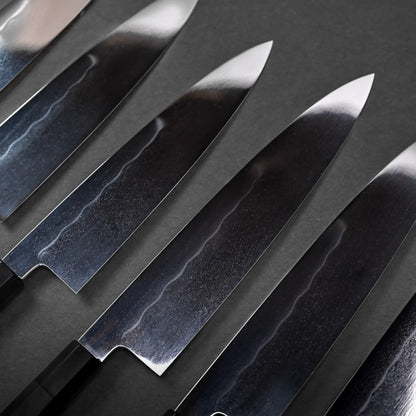 A row of gyuto blades with a mirrored finish, Japanese knife handles not visible, showing classic chef's knife shapes.