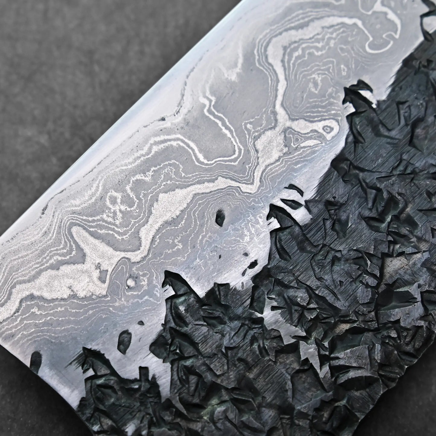 Swirling damascus steel patterns and jagged black edge on a Japanese knife blade visible in close-up.