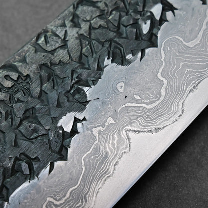 Close-up of a Japanese knife blade showing Damascus steel with wavy and geometric patterns, blade shape not visible.