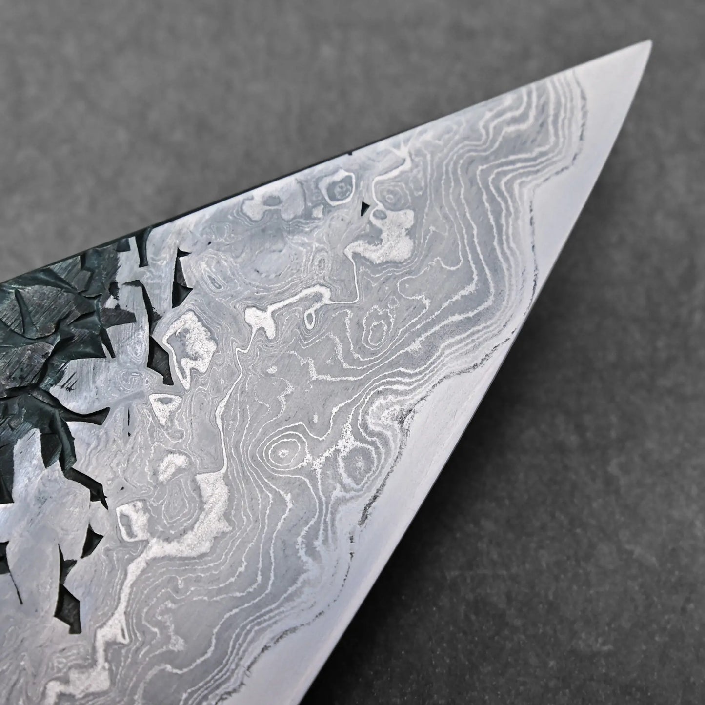 Close-up of the tip showing wavy Damascus pattern on a Japanese knife blade; specific type not discernible.