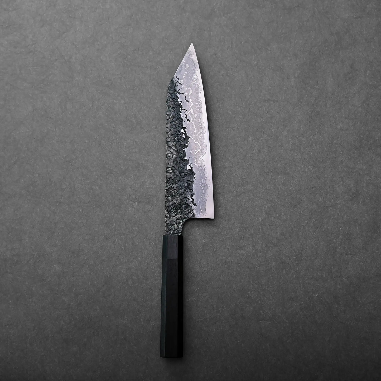 A Japanese knife with a kiritsuke gyuto shape, featuring a textured, patterned blade and black handle.