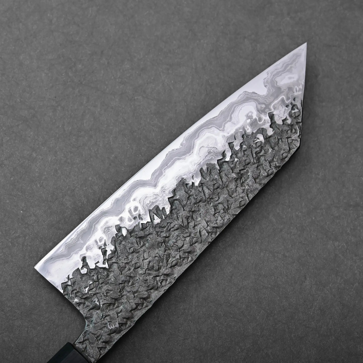 Close-up showing the textured damascus steel pattern of a Japanese knife, specifically a Kisuke Manaka bunka blade.