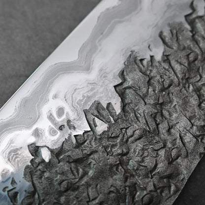 Close-up of a blade showing textured, patterned steel and contrasting finishes on this Japanese knife.