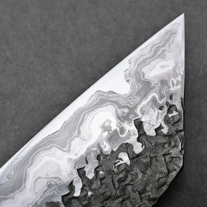 Close-up showing a Japanese knife blade with wavy Aogami #1 damascus layers and a dark, textured lower section.