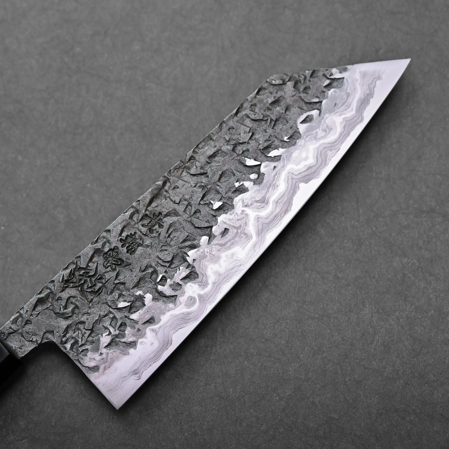 A macro shot showing a patterned blade section of a Japanese knife, with the overall blade shape not visible.