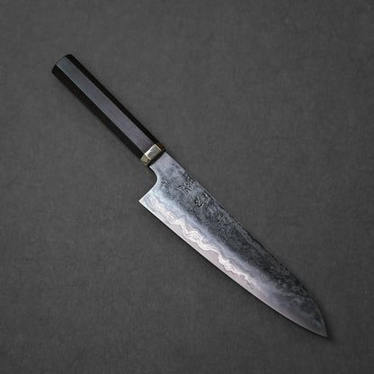 Japanese chef’s knife with Damascus steel blade featuring intricate layered forge patterns, vertically engraved kanji characters, and a dark wooden handle with brass bolster; photographed against a textured backdrop.