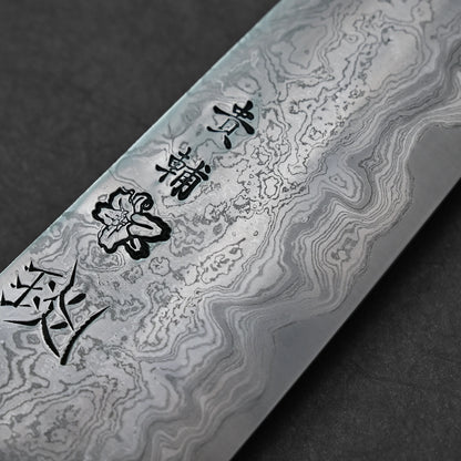 Japanese Damascus steel knife blade featuring layered wavy forge patterns, vertically engraved kanji characters, and a delicate flower motif etched near the center.