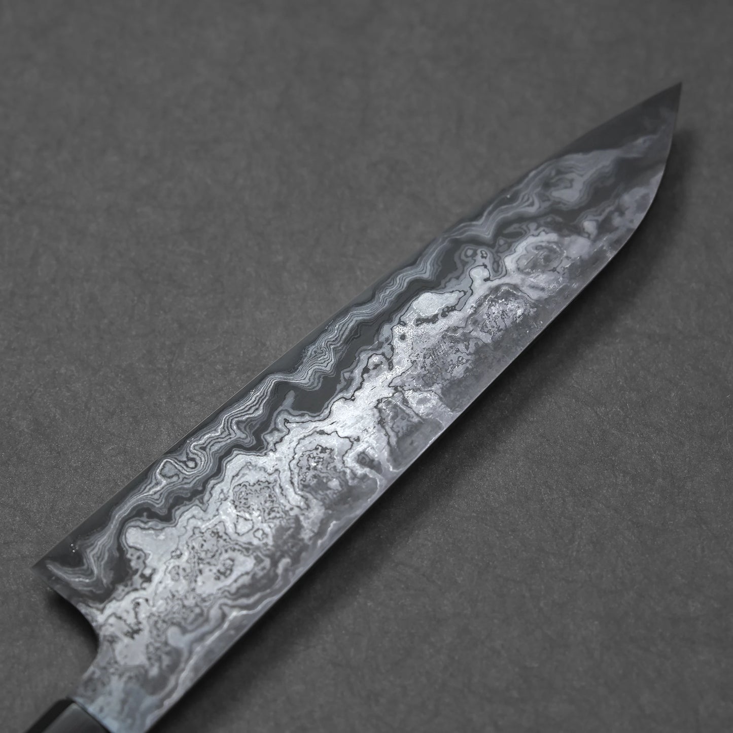 Close-up of a Damascus steel knife blade showcasing fine wavy forge patterns and subtle, layered texture.