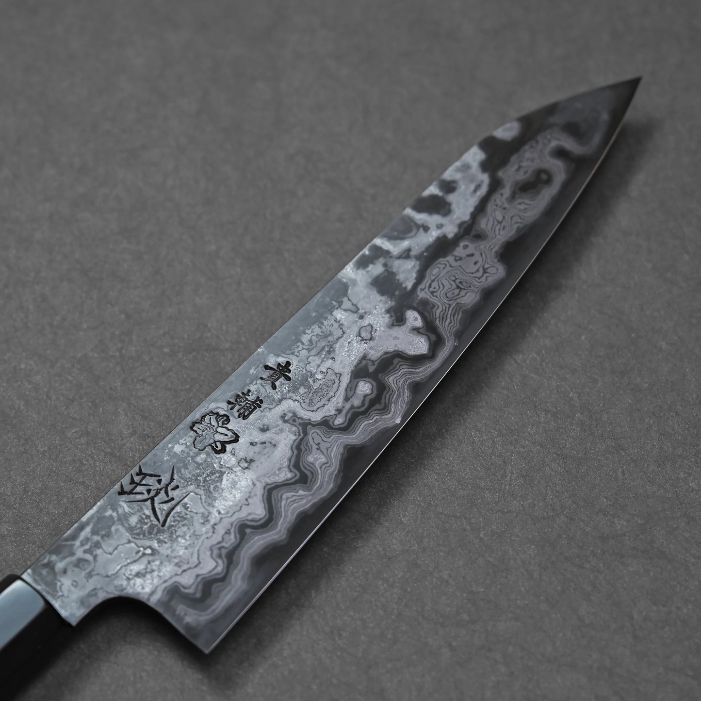 Close-up of a Damascus steel knife blade with wavy forged patterns and engraved Japanese kanji characters.