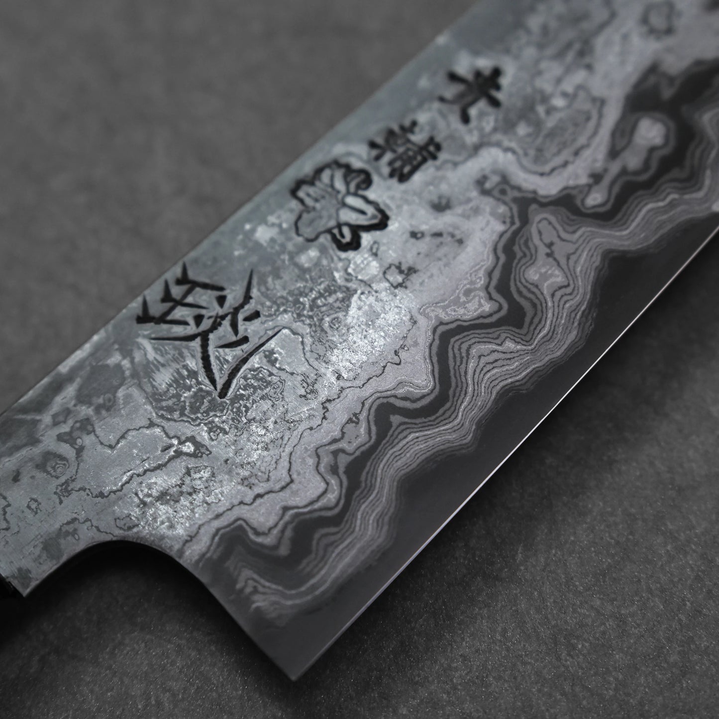 Close-up of a Damascus steel knife blade with engraved patterns on a dark background