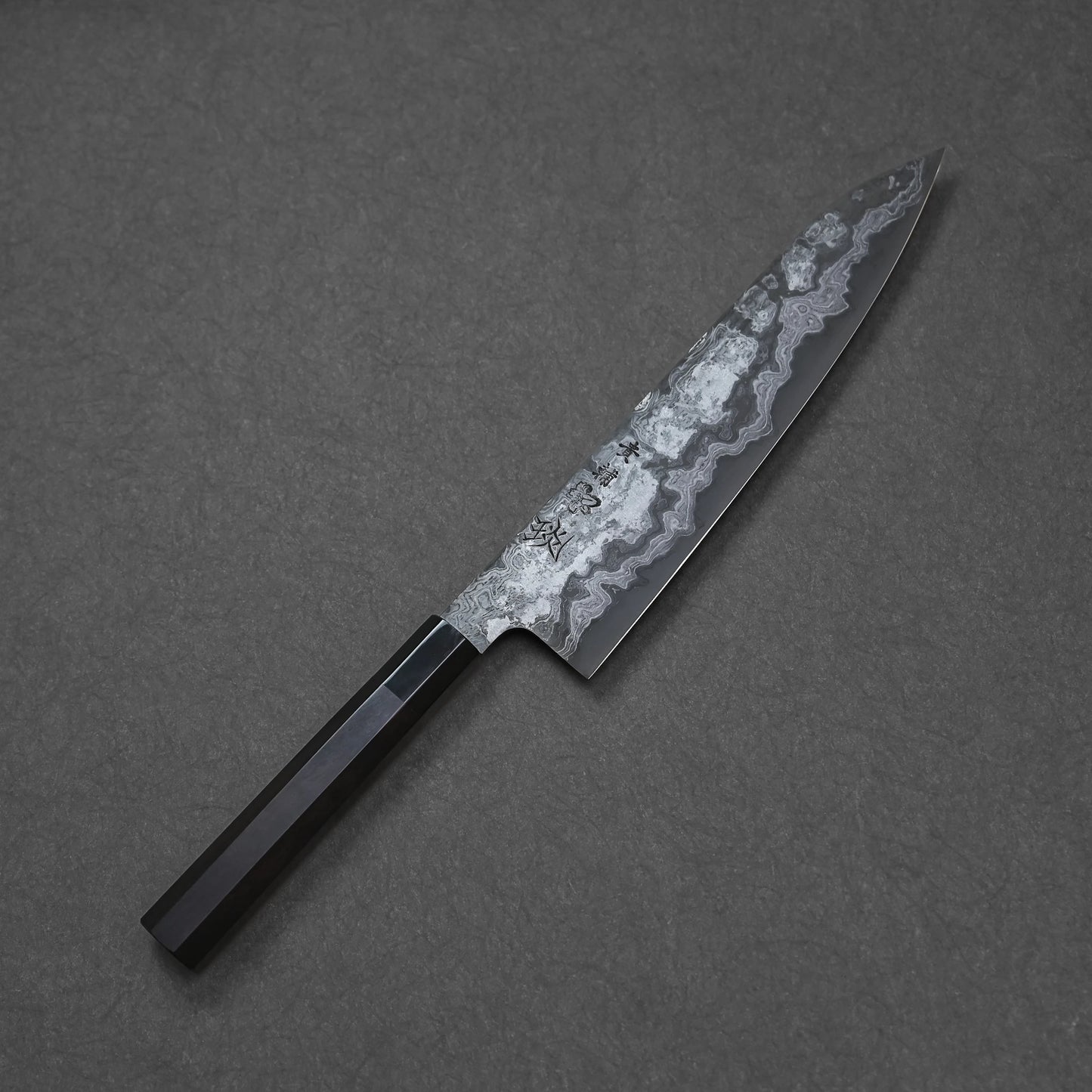 Damascus chef's knife with a black handle on a gray background