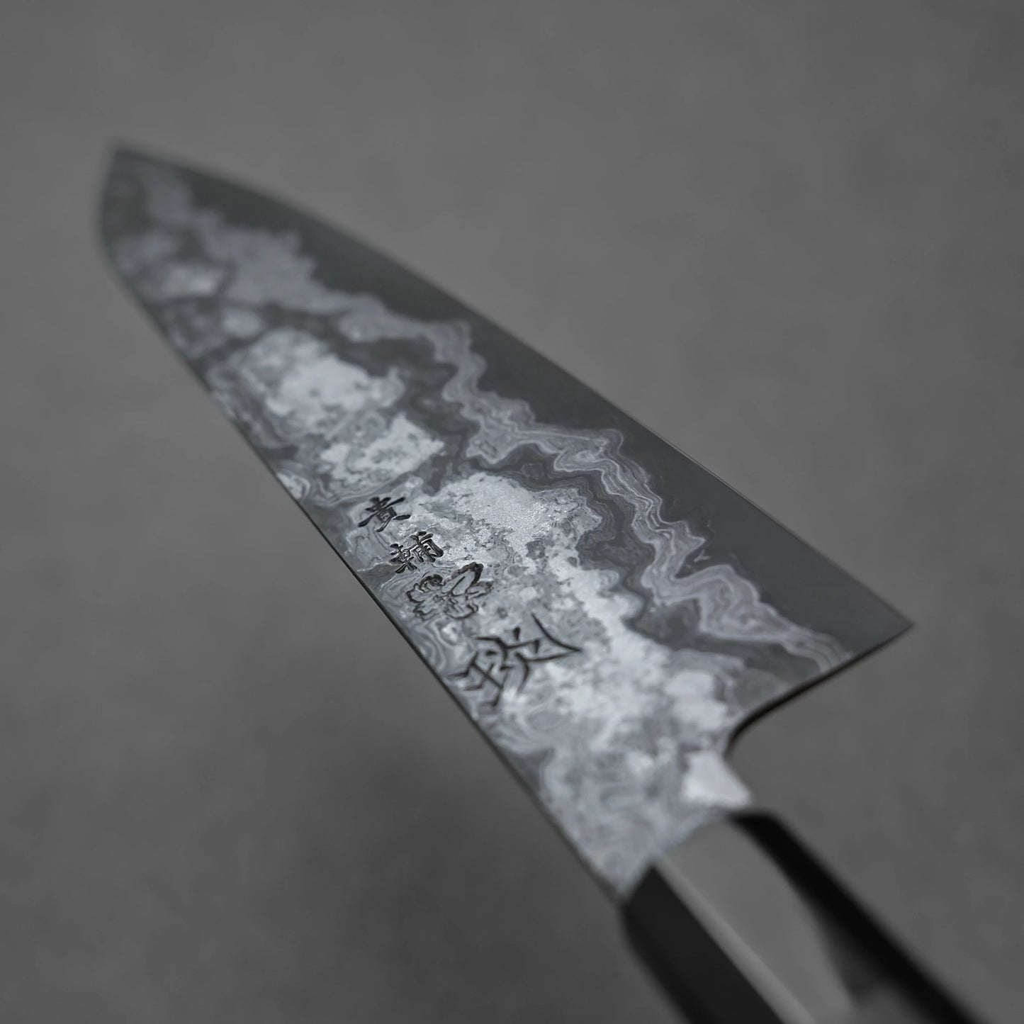 Close-up of a chef's knife with a textured blade on a dark background