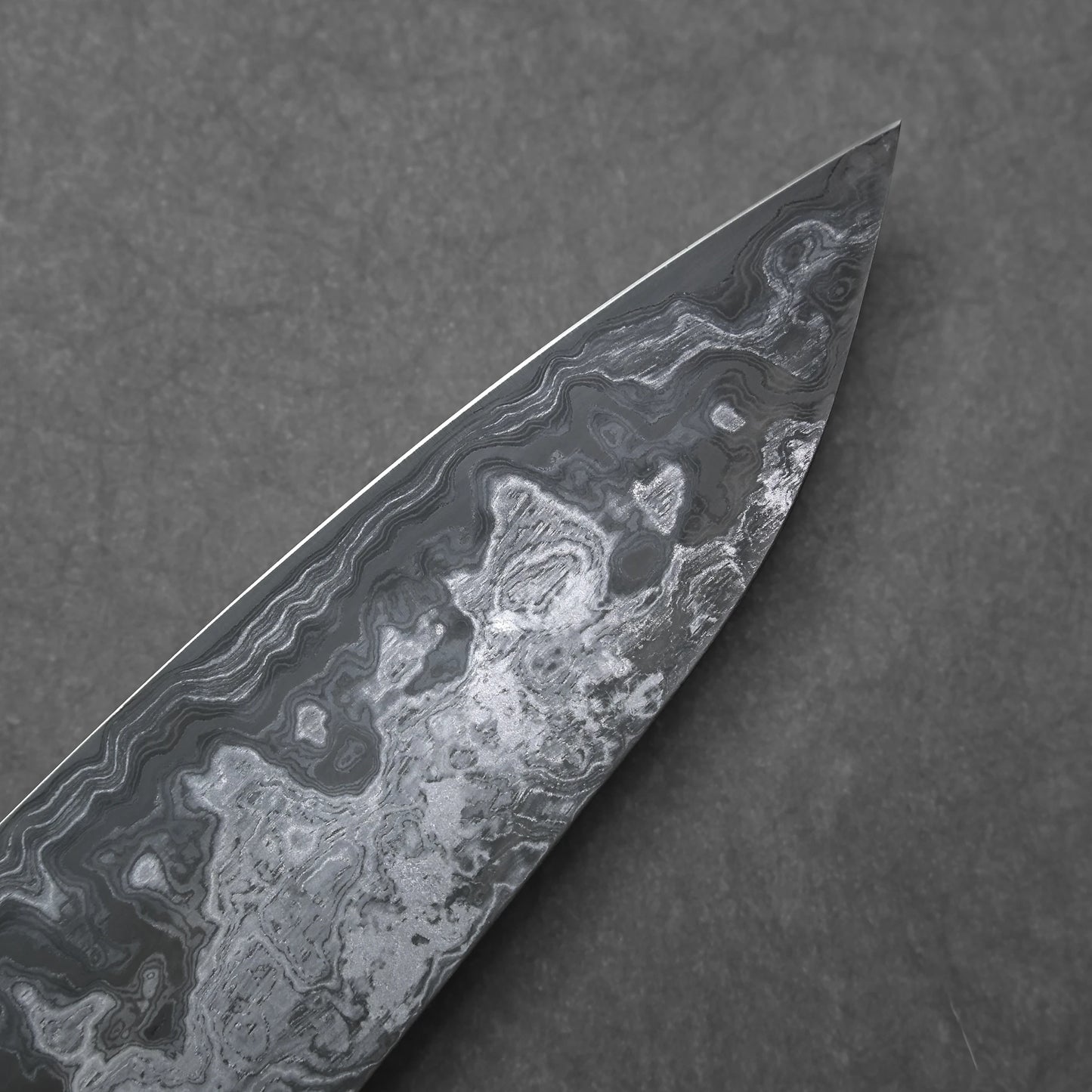 Close-up of a knife blade tip with a marbled damascus pattern on a dark gray background