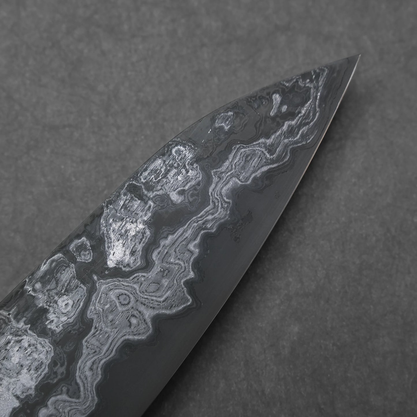 Close-up of a knife blade tip with a unique pattern on a dark background