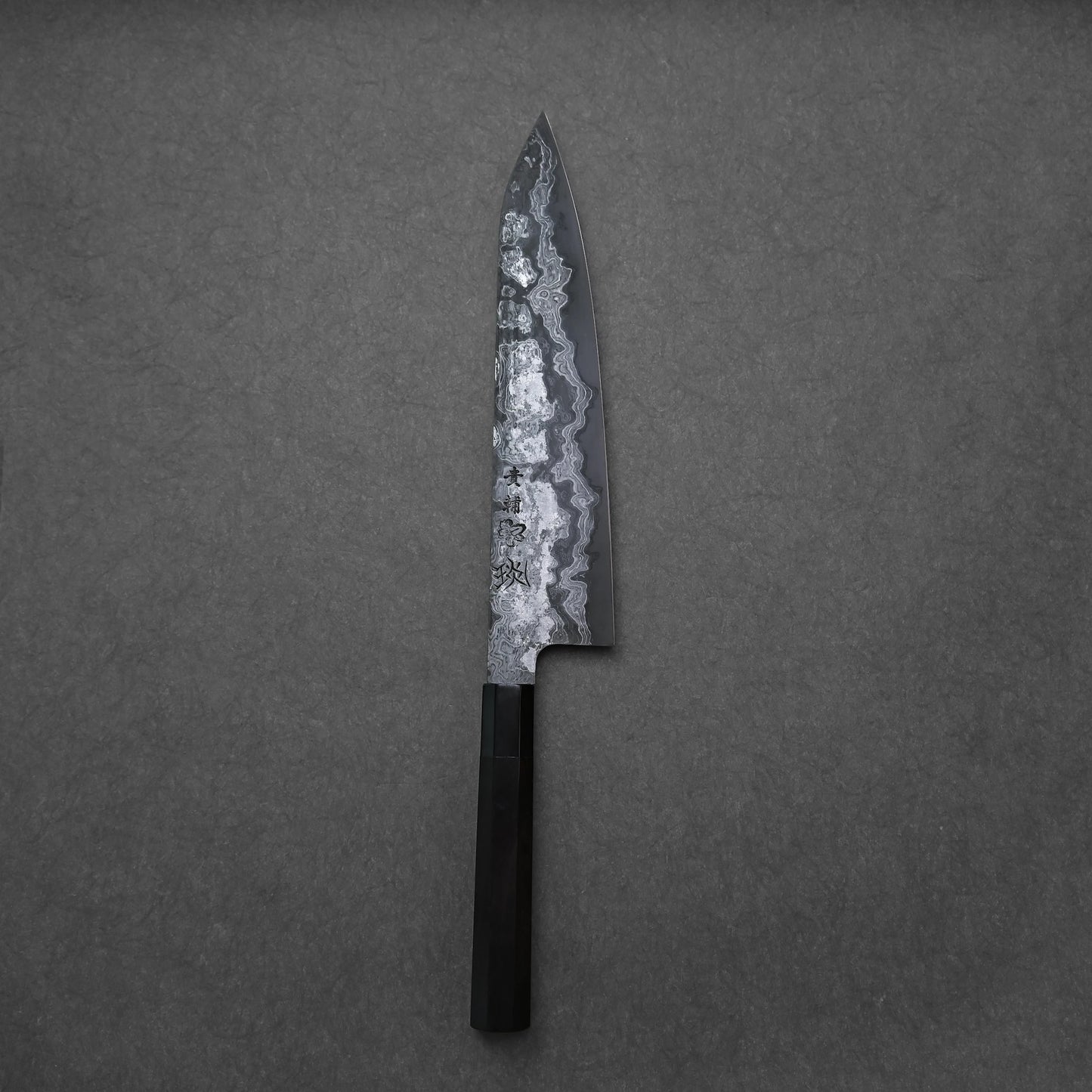 Damascus gyuto with a black handle and etched blade on a gray background