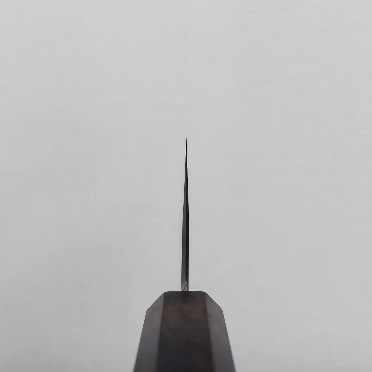 Choil shot of a Miyazaki ATS34 bunka knife blade, with the edge facing upward and tapering to a point against a plain, light gray background.