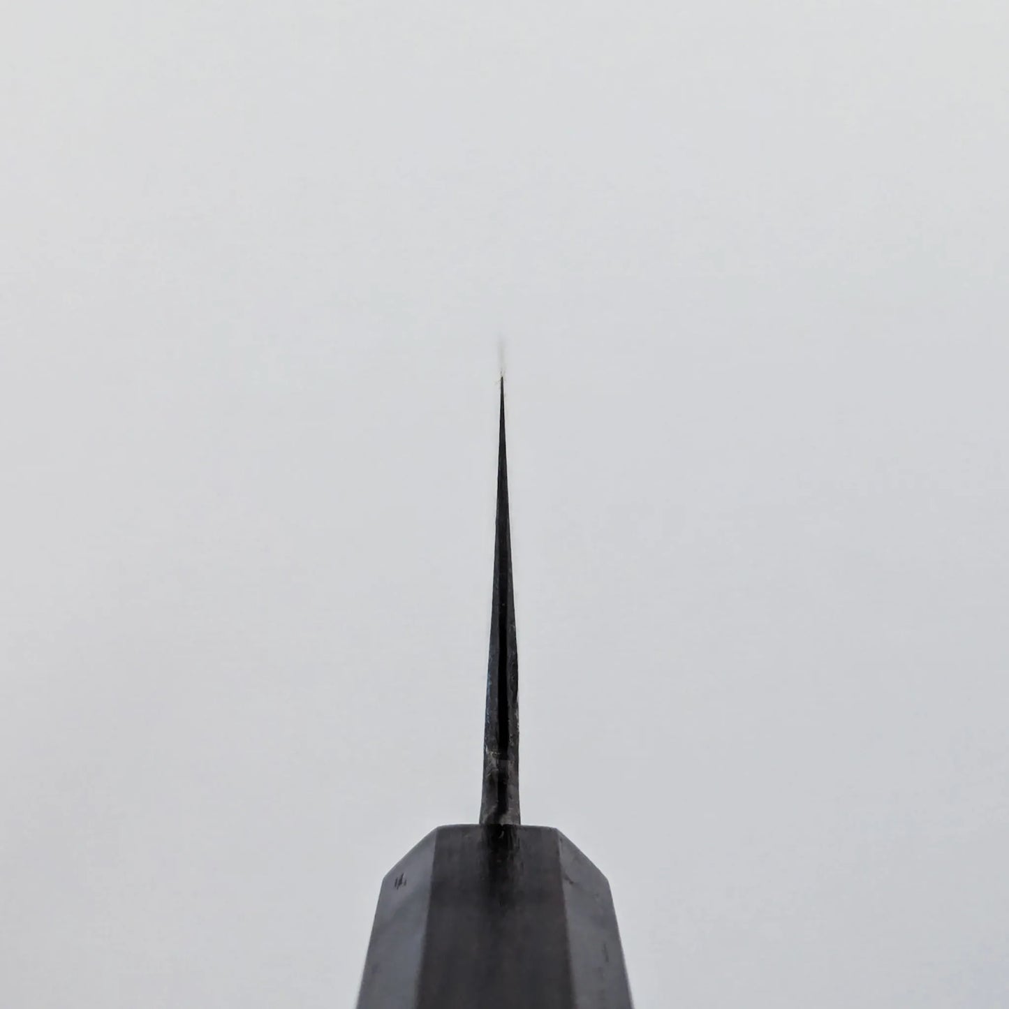 Choil shot of a knife viewed from the handle, with the blade positioned vertically against a plain white background.