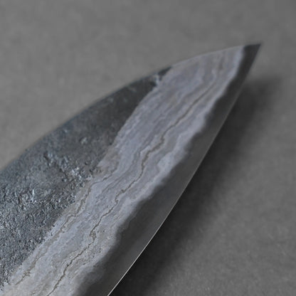 Close-up of a knife blade revealing a wavy, patterned texture along the metal edge, highlighting a classic Damascus steel design against a gray background.