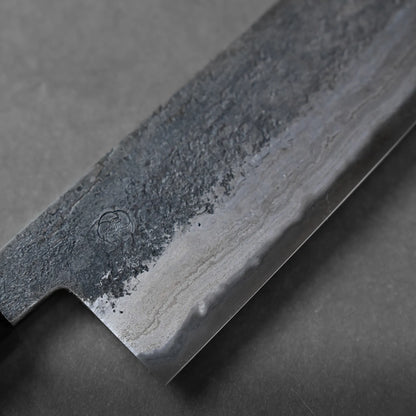 Close-up of a knife blade displaying a textured, dark upper section and a polished edge with visible layers, resting on a gray surface.