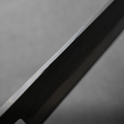 Close-up view of the edge of a metal knife blade against a plain grey background.