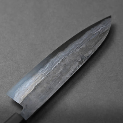 A close-up of a chef’s knife blade with mesmerizing wavy patterns, likely crafted from Damascus steel, set against a plain gray background.