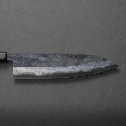 A close-up view of a chef’s knife blade featuring a wavy, patterned texture, set against a plain grey background. The unique pattern enhances the blade's visual appeal.