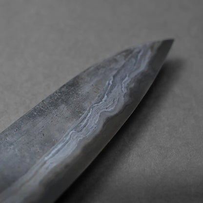 A close-up view of the tip of a Damascus steel chef's knife blade, showing distinctive wavy patterns on the metal surface against a neutral gray background.