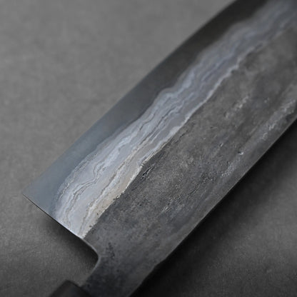 Close-up of a Damascus steel knife blade with visible layered patterns in dark and light gray tones. The background is a smooth, solid gray surface.