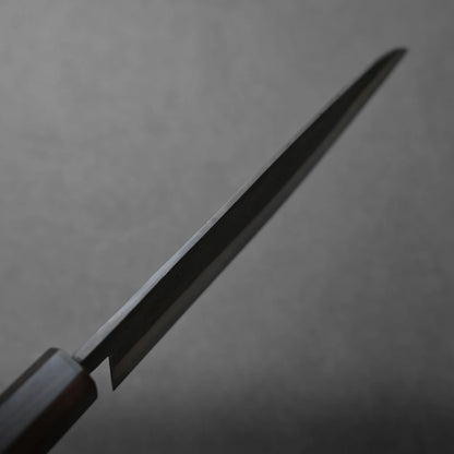 A close-up photo of a kitchen knife blade angled upward against a plain, blurred gray background. The handle appears partially visible on the left side of the image.