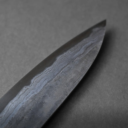 Close-up of the tip of a Damascus steel knife blade featuring distinctive wavy patterns and a matte finish, highlighting its craftsmanship against a gray background.