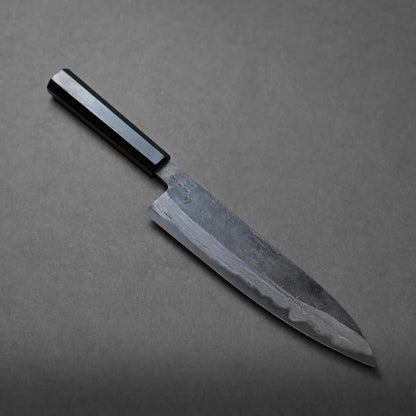 A Japanese-style chefs knife with a dark wooden handle and a slightly curved blade rests on a plain gray surface.