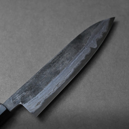 A close-up view of a Japanese chef’s knife with a damascus-patterned blade resting on a gray surface. The edge and unique texture of the blade are clearly visible.