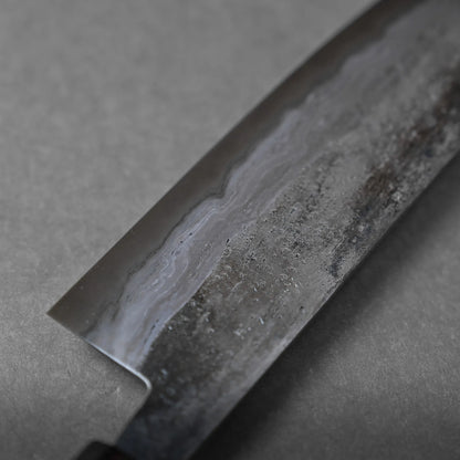 Close-up of a kitchen knife blade featuring a wavy pattern and textured surface, characteristic of Damascus steel, set against a gray background.