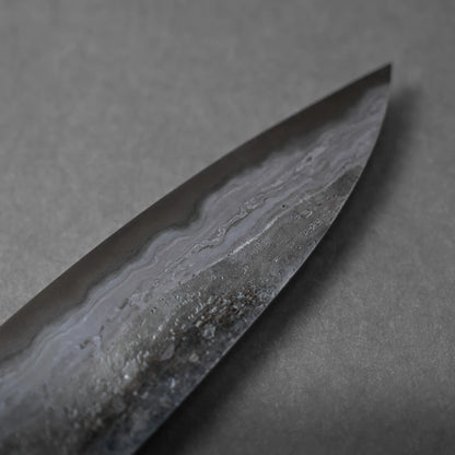 Close-up of the pointed tip of a Damascus steel knife blade, highlighting distinctive wavy patterns and intricate texture on the metal, set against a plain grey background.