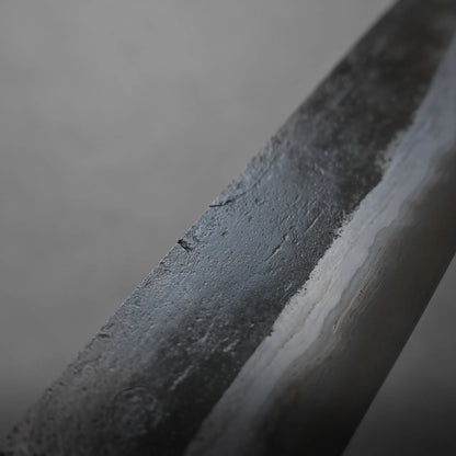 Close-up of a metal blade displaying a textured, two-toned pattern and layered structure, set against a gray, blurred background. The focus is on the blade’s intricate surface details.