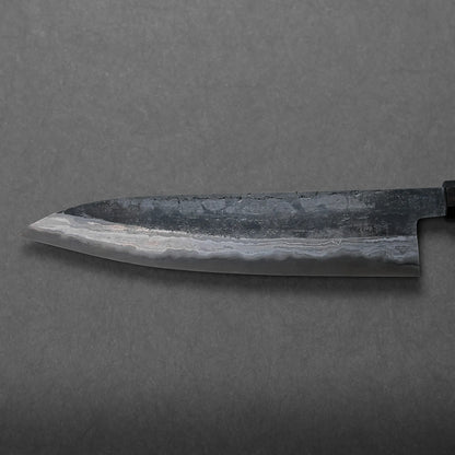A close-up view of a Japanese-style chef’s knife featuring a dark, patterned blade and a straight edge, set against a plain gray background for an elegant display.