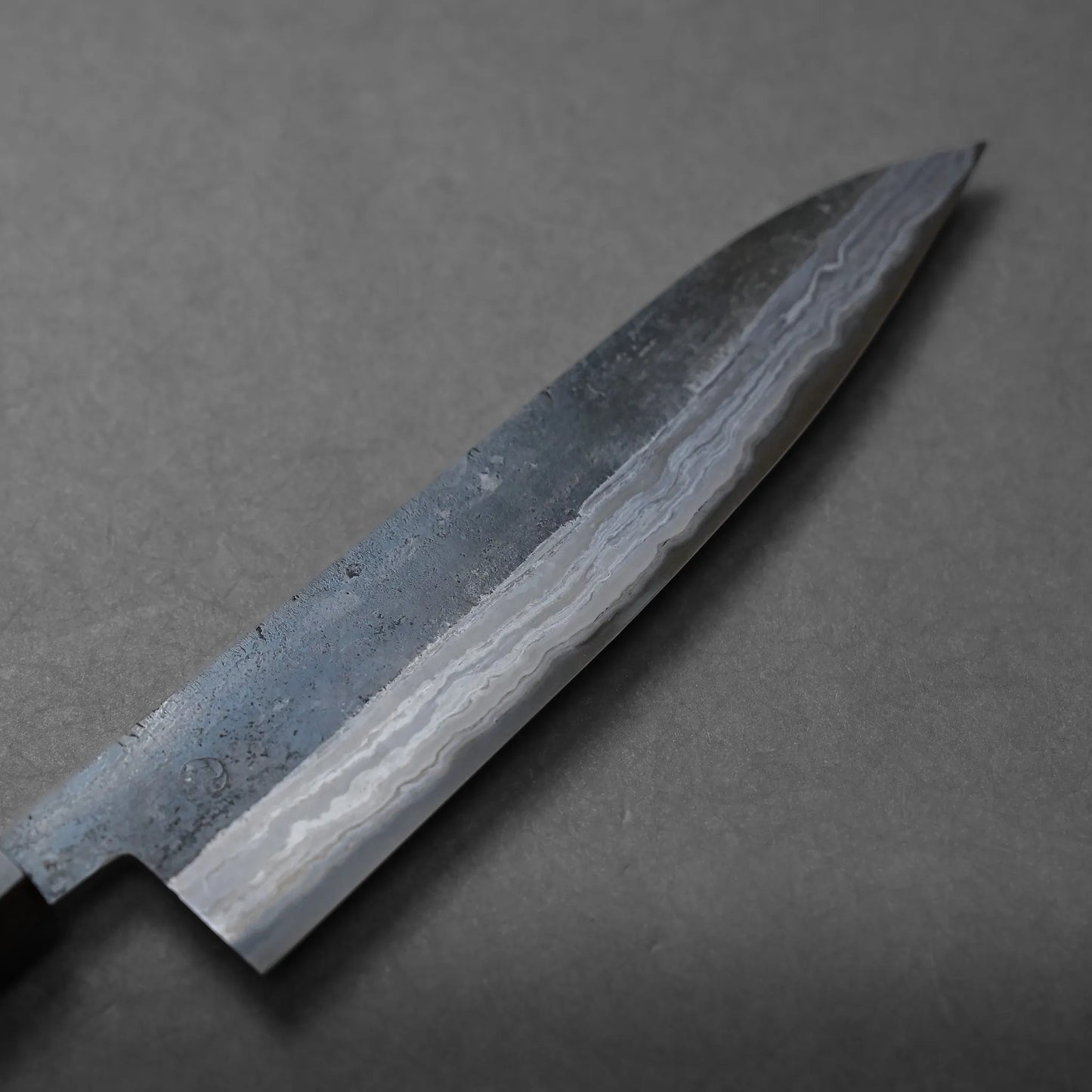 A close-up of a Japanese-style chef’s knife with a patterned Damascus blade, shown against a plain gray background.