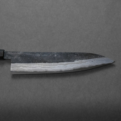 Close-up of a Japanese-style kitchen knife with a dark blade showcasing a striking wavy pattern along the edge, set against a plain gray background.