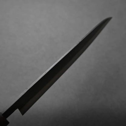A close-up view of a kitchen knife blade set against a plain, gray background. The blade is angled diagonally across the image, showcasing its thin, pointed edge.